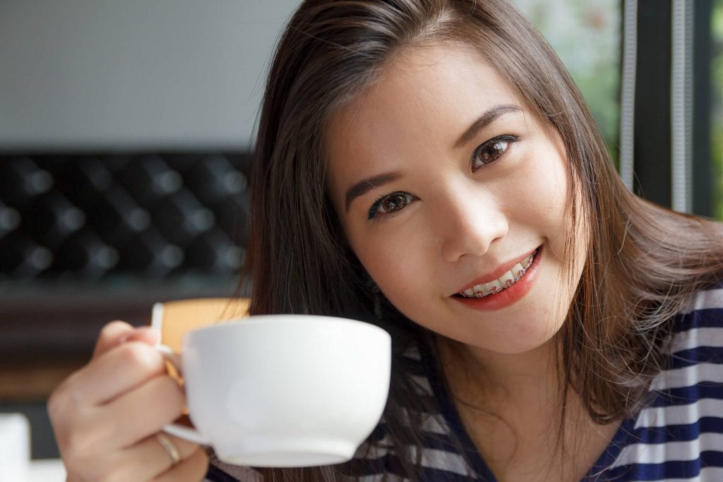 a woman smiling her braced teeth and holding a cup