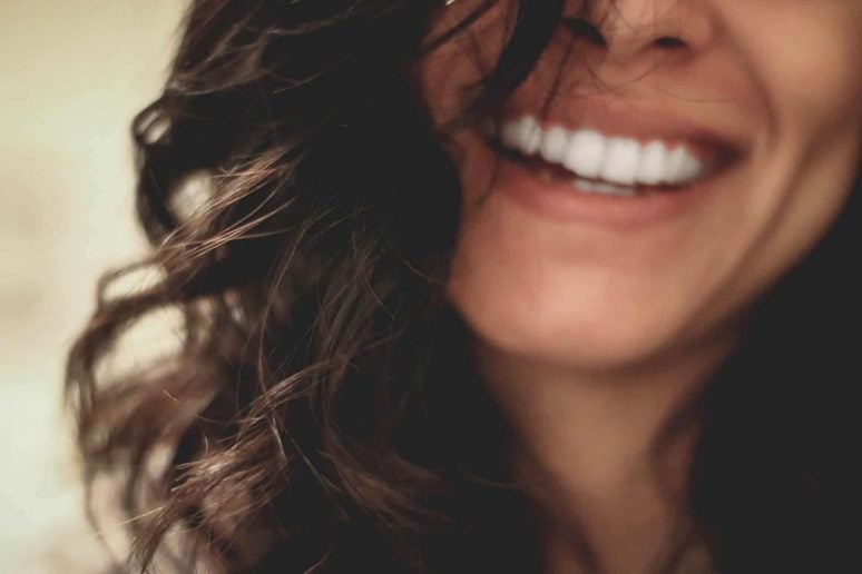 Faded photo of a woman smiling with her teeth after a visit to the dentist