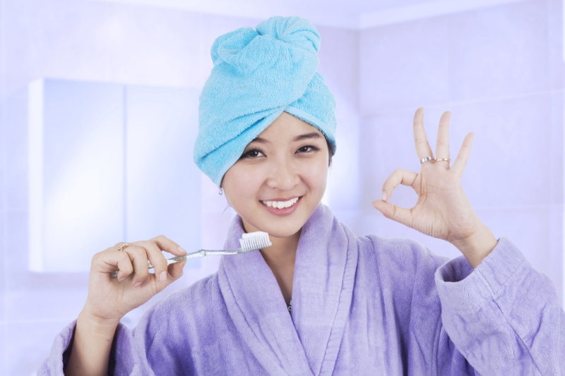 Girl brushing her teeth and showing ok gesture