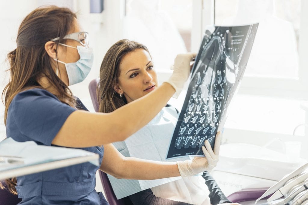 Dentist talking with her patient and teaching a radiograph.